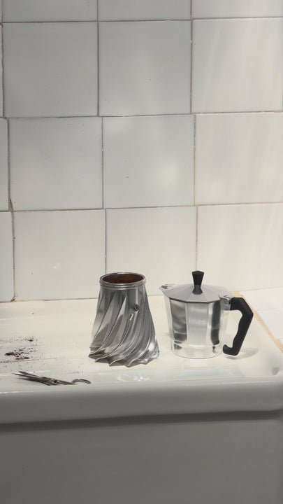Hands assembling the Turbo Moka at the sink, screwing the fluted boiler into the top chamber