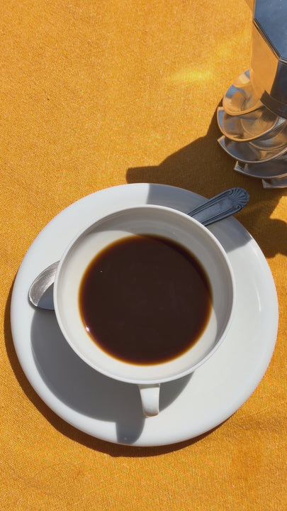 Overhead view of milk poured from an enamel jug into a cup of Turbo Moka coffee on a yellow surface